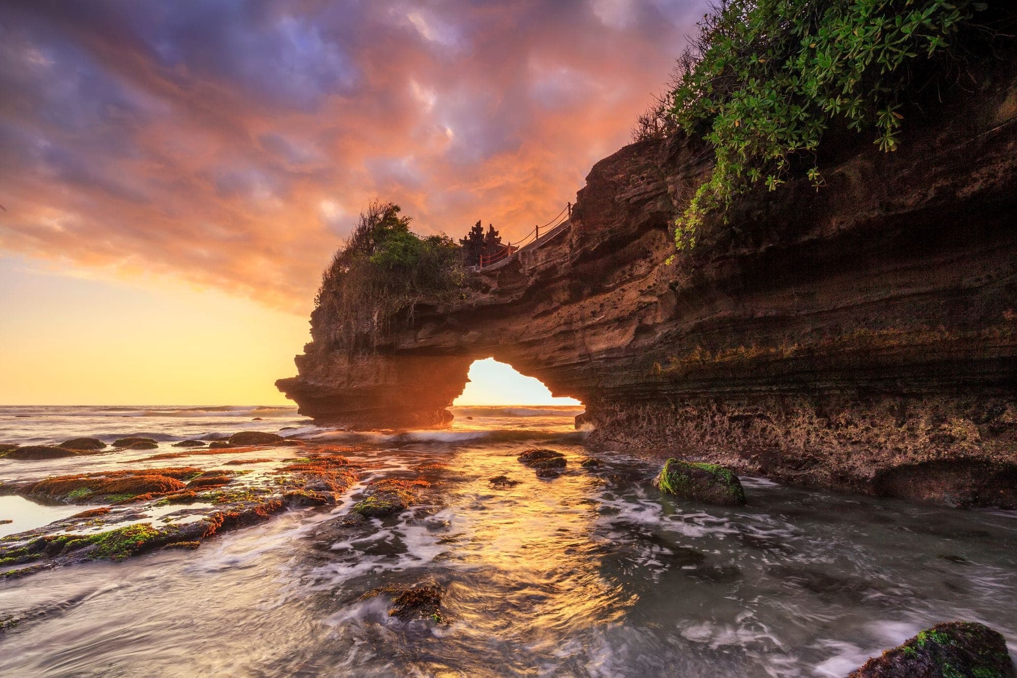 Rock sea arch with a small temple above the Indian Ocean at sunset, Bali